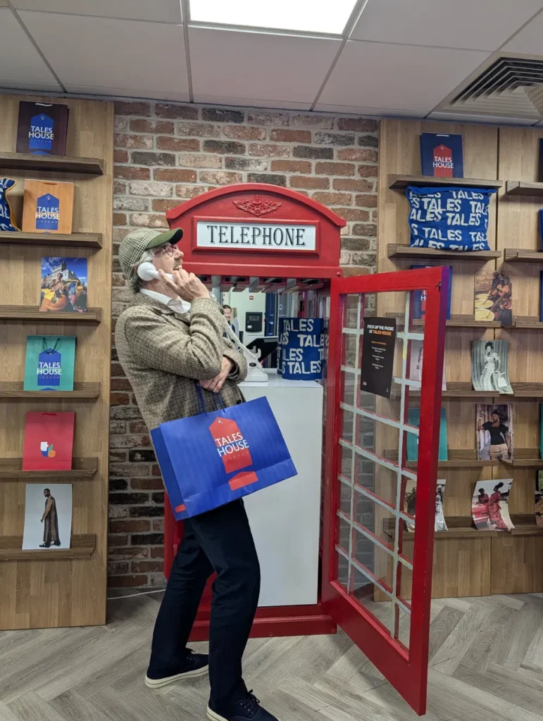 A visitor on the vintage white telephone inside the red phone box at TALES House, carrying a TALES House shopping bag